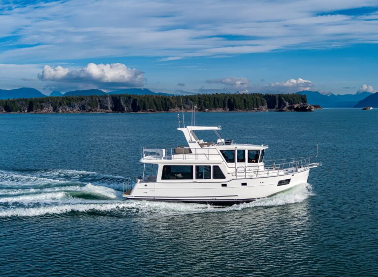 North Pacific custom trawler yacht cruising on calm blue water near forested coastline