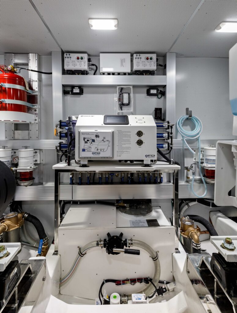 Organized yacht engine room with equipment mounted on the systems wall and a red portable fire extinguisher at left