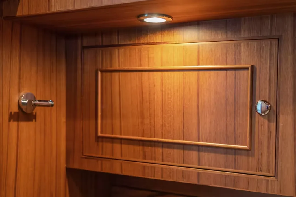 Wooden storage cabinet with polished chrome latch and overhead light on a yacht