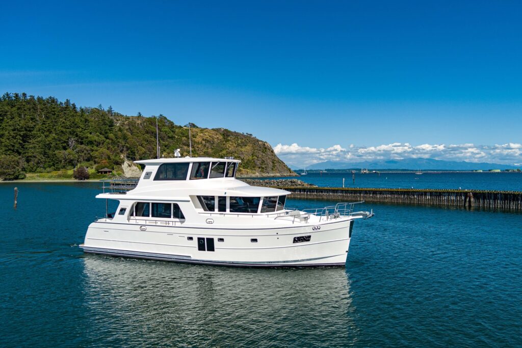 White North Pacific pilothouse yacht cruising past a forested shoreline