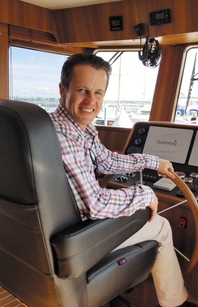 Man smiling at the helm of a pilothouse yacht with Garmin navigation equipment