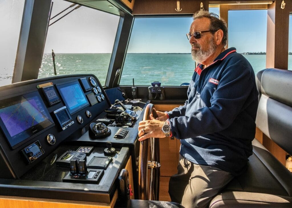 Man navigating North Pacific Yacht pilothouse with advanced marine electronics and steering wheel