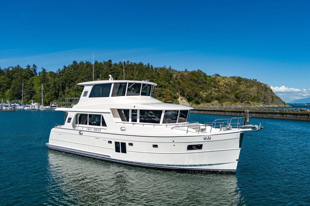 White North Pacific pilothouse yacht cruising near a forested shoreline