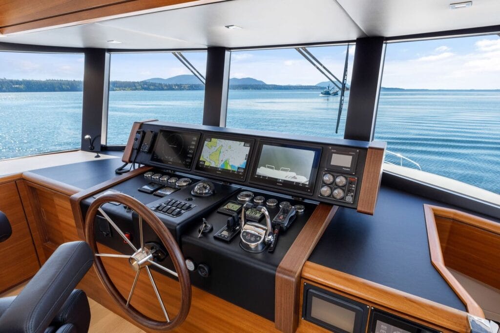 Pilothouse helm aboard a North Pacific Yacht with navigation displays, a wooden steering wheel, and open water ahead